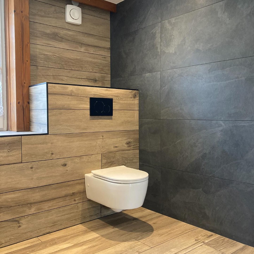 WC suspendu et faïence sombre dans la salle de bains rénovée